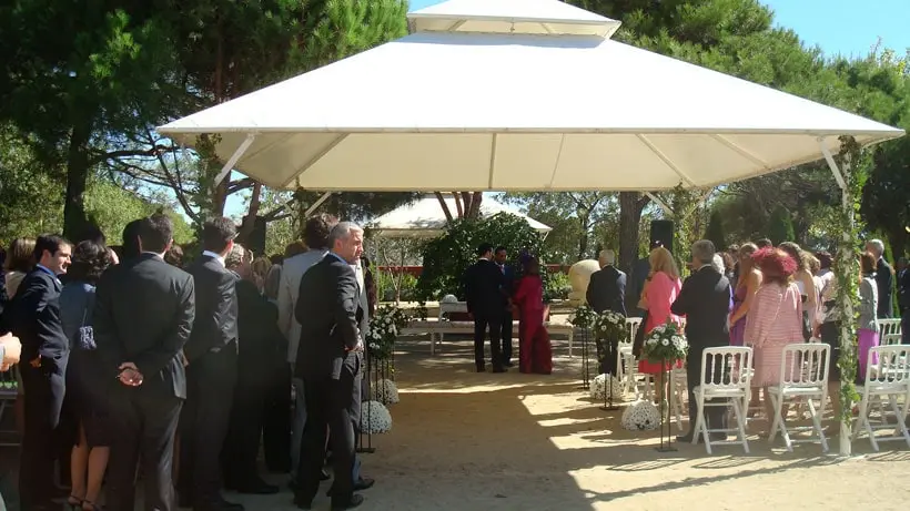 Invitados reunidos bajo el cenador blanco para una ceremonia en el jardín