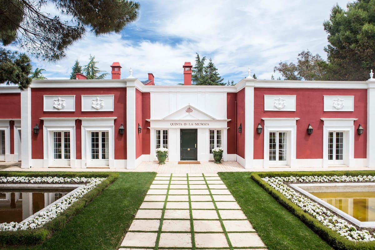 La fachada roja y blanca de la Quinta La Muñoza, con su parterre de boj, dos estanques y los pinos alrededor